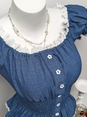 Blue denim maternity blouse with puff sleeves, lace trim, and decorative flower buttons.