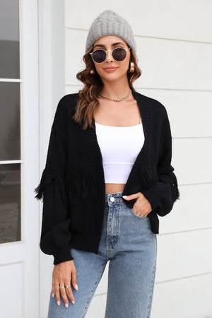 Black acrylic cardigan with fringe detail on sleeves and open front, styled with a white crop top and jeans.