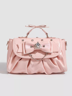 Pink ruched crossbody bag with bow, crown charm, and chain detail.