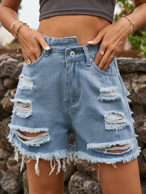 Distressed denim cutoff shorts in dusty blue with an asymmetric waist and frayed hem.