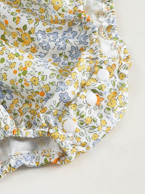 Baby one-piece with white floral print, yellow, blue, and orange flowers, and white buttons.