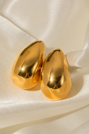 Sculptural gold teardrop stud earrings with a polished finish on satin fabric.