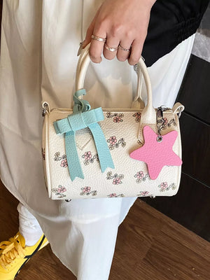 Charming floral mini crossbody bag in white with pink flowers, blue bow, and pink star charm.