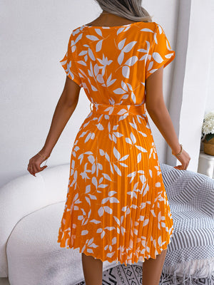 Orange midi dress with white leaf print, short sleeves, belted waist, and pleated skirt.
