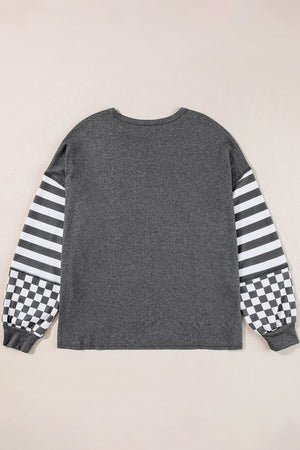 Asymmetrical knit top in charcoal gray with striped and checkered patchwork sleeves.