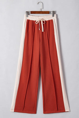 Terracotta-red track pants with cream side panels and drawstring waist
