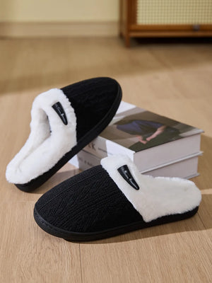 Black cable knit house slippers with white shearling lining and a decorative button.
