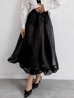 Black midi skirt with sheer overlay and elastic waistband, styled with heels.