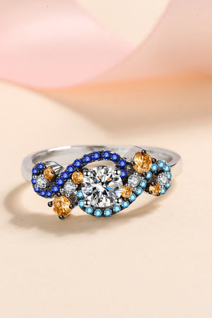 Silver ring with a central diamond and swirling blue, gold, and clear gemstones.