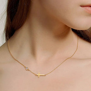 Gold asymmetrical cross pendant necklace with a single clear stone.