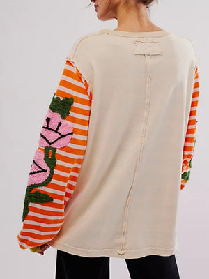 Beige long sleeve tee with orange striped sleeves featuring embroidered floral appliques.