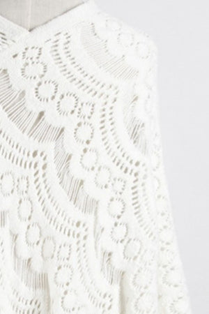 White crochet poncho with intricate openwork pattern and fringe detail.