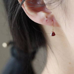 Dainty gold drop earrings with a single red heart-shaped zircon gem.