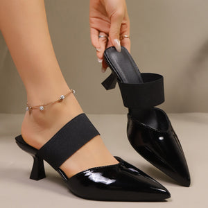 Black patent pointed toe mules with elastic strap and sculpted mid-heel.