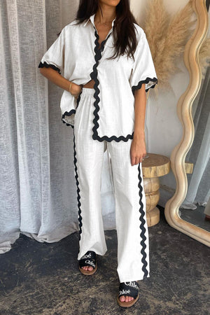 White linen co-ord set with black scalloped trim on shirt and pants.
