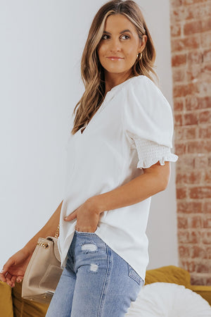 White puff sleeve V-neck blouse with smocked cuffs and ruffle trim.