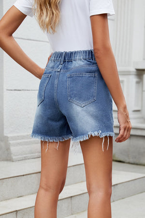 Distressed denim shorts in dusty blue with an asymmetric elastic waistline and frayed hem.