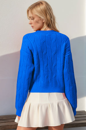 Blue cable knit sweater with crew neck and long sleeves, detailed with a bow embellishment.