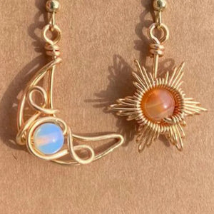 Gold celestial asymmetrical drop earrings with moon and sun charms and gemstone accents.
