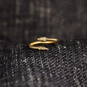 Gold bypass snake ring with diamond accents and green eye detail
