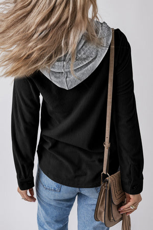 Black corduroy shirt jacket with contrast gray hood and button cuffs, styled with jeans.