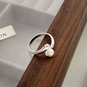 Silver bypass ring with a single pearl accent, delicate and modern design.