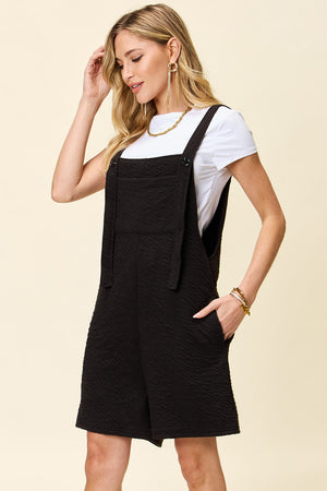 Textured black bib short romper with pockets and button details.