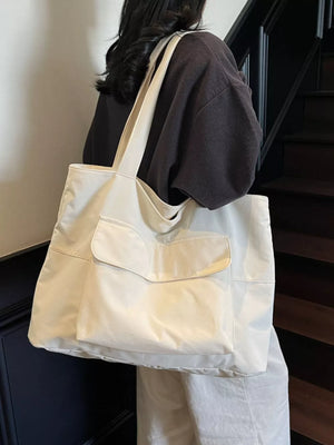 Spacious cream nylon shoulder bag with flap and front pockets, worn by a woman.