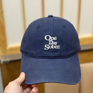 Navy blue cotton baseball cap with embroidered "One Day Sober" text and distressed finish.