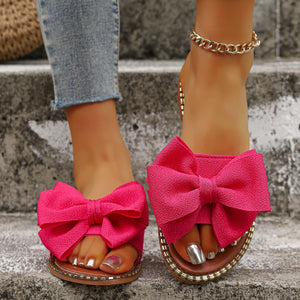 Fuchsia pink bowknot sandals with gold trim detail, worn with jeans and a gold anklet.
