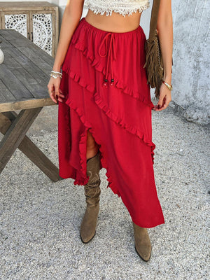 Scarlet midi skirt with cascading ruffles and a thigh-high slit, styled with boots.