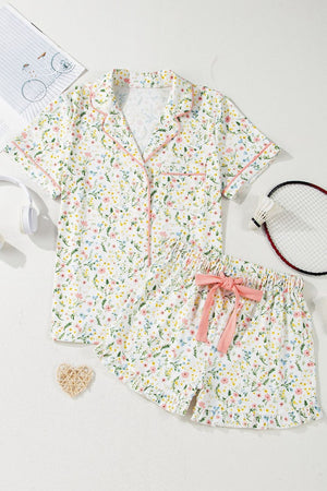 Floral print pajama set with pink trim, button-up top and ruffled shorts with bow.