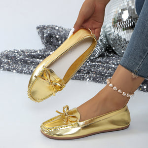 Gold bow embellished flat slip-on loafers with a rounded toe and decorative stitching.