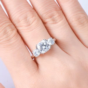 Silver three-stone cushion cut moissanite ring with a central large stone and two smaller side stones.