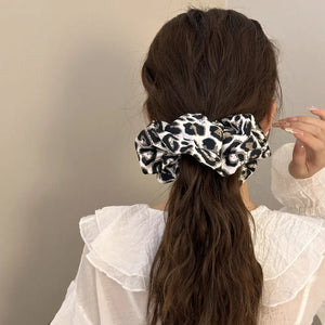 Leopard print silk scrunchie in tan and white, holding a ponytail.