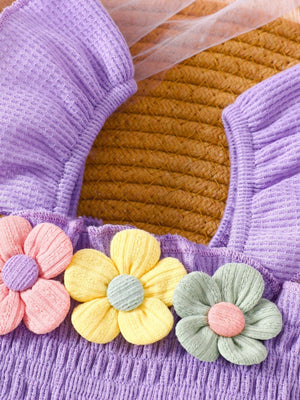 Purple smocked jumpsuit with floral appliques in pink, yellow, and pastel blue.