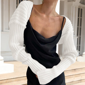 White ribbed knit sleeve shrug with long sleeves and a casual cut, worn over a black dress.