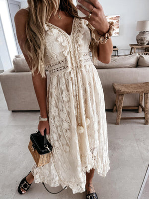 Beige lace V-neck maxi dress with ruffles, tassels, and pom-poms.