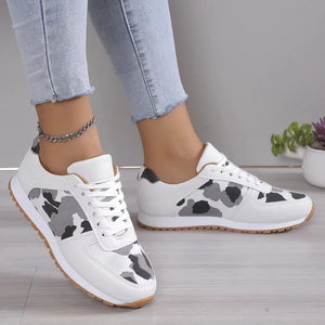 White sneakers with black and grey camouflage print panels and gum soles.