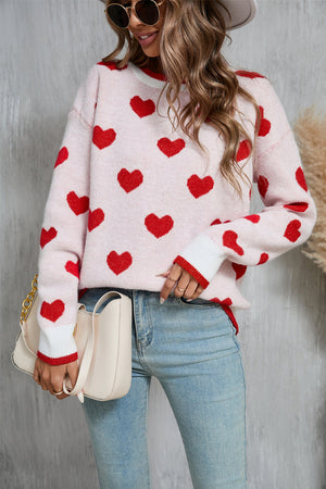 Pink crewneck sweater with red heart intarsia pattern and white cuffs.