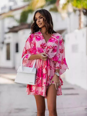Tropical tiered mini dress in fuchsia pink with a floral print, V-neck, and tie waist.