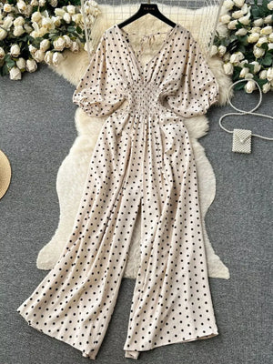 Beige polka dot smocked wide-leg romper with V-neck and tie detail.