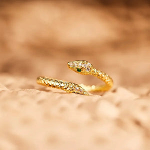 Gold bypass ring with diamond accents and a green eye, shaped like a serpent.