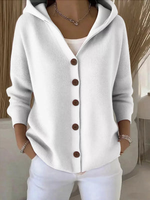 White hooded button-front knit cardigan with brown buttons, styled with a white tank and white pants.