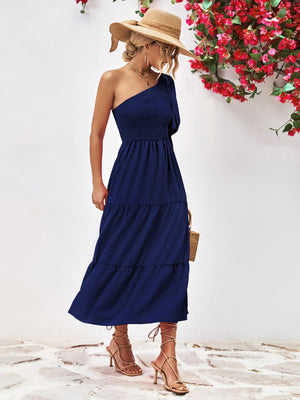 Dark blue smocked bodice tiered one-shoulder midi dress with a straw hat and sandals.