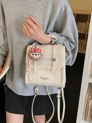 Chic mini flap backpack in white with plush charm and adjustable strap.