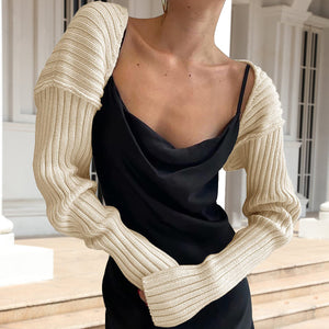 Ribbed knit shrug with extended sleeves in Sand, worn over a black slip dress.