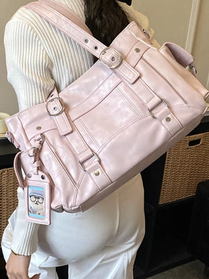 Pink shoulder bag with buckle and strap details, worn by a woman.