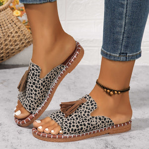 Tassel-embellished open-toe slide sandals in white leopard print with decorative stitching.