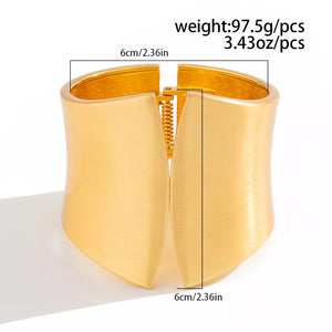 Gold-toned sculptural cuff bracelet with a wide, open design and spring hinge closure.